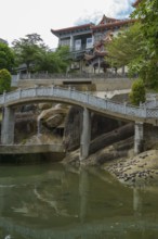 Stone bridge over pond leads to traditional temple complex, penang, malaysia