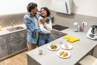 Young loving couple hugging in their modern kitchen with breakfast pastries and strawberries on the