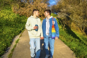 Young caucasian gay couple holding hands and walking in a park, enjoying a sunny day together