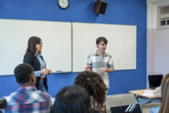 Teenage student giving a presentation in a modern classroom with a teacher and diverse group of