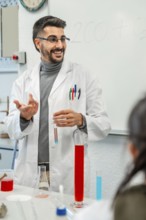 Smiling chemistry teacher showing colorful test tubes and beakers while explaining chemical