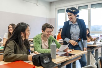 Happy teacher assisting college students learning and preparing exam in university classroom