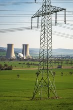 An electricity pylon stands in a green landscape with the Grohnde nuclear power plant in the