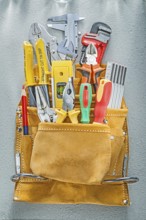 Assortment of construction tooling in tool belt on concrete background