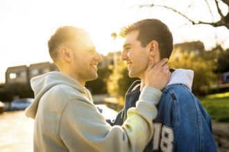 Two men are embracing and smiling at each other in the golden light of sunset, enjoying a tender