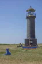 Brick lighthouse next to boat and blue sculpture in a meadow under blue sky, juist, north sea,