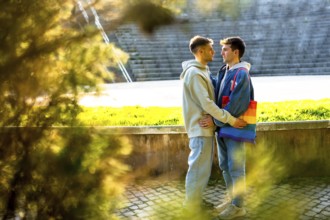 Two men embracing in a park, one showcasing a vibrant rainbow bag, celebrating lgbtq plus pride,