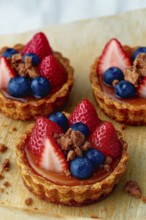 Three delicious fruit tarts featuring fresh strawberries, blueberries, and crumble toppings on a