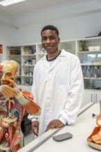 Young scientist wearing lab coat standing next to anatomical model in university laboratory