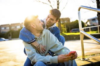 Two men are hugging and laughing while looking at each other, one of them is holding a smartphone