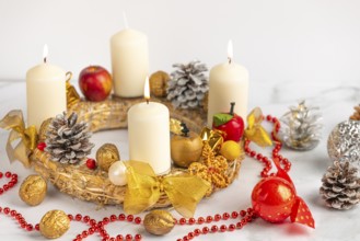 Advent wreath with three burning candles, red pearl necklace and Christmas decorations next to it