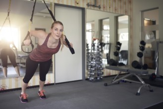 Young fit blond woman exercising with suspension bands in a modern gym in the morning