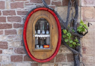 Wine bottles from the Alte Kelter winery in a wine barrel with a glass window on a house wall with