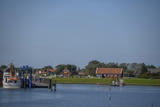 Small boats and traditional buildings at the harbour with calm water and blue sky, langeoog, east