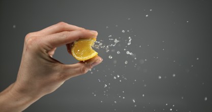Hand of Woman Squeezing Orange against Black Background