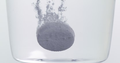 Tablets Falling and Dissolving into a Glass of Water against White Background