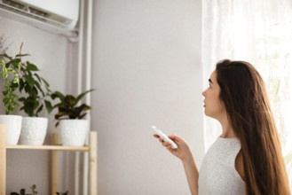 Young woman adjusts the temperature of the air conditioner using the remote control in room with a