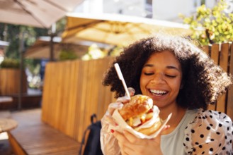 Young african american girl eating classic burger and drinking lemonade in the city. Outdoor woman