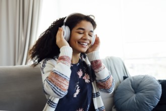African millennial woman in orange sweater wearing white wireless headphones, listening music,