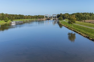 A water channel with a lock and bridge, surrounded by nature under an expansive sky