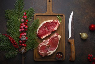 Two raw uncooked meat beef steaks on wooden cutting board with knife and seasonings on dark rustic