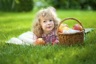Happy smiling child eating apple outdoors in spring park