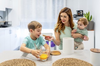 Happy woman feeding her son while holding a baby during breakfast at home