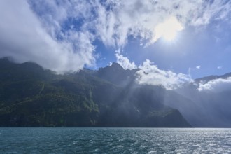 Sunshine over mountains with partial cloud cover and blue water, summer, Milford Sound, Te Anau,