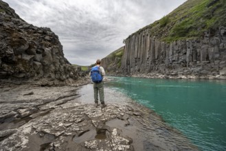 Tourist standing by the river in Stuðlagil Canyon, turquoise blue river between basalt columns,