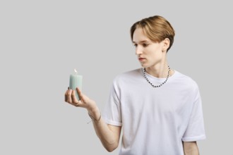 Young man holds candle in hand over grey studio background