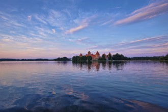 Trakai Island Castle in lake Galve, Lithuania on sunset with dramatic sky reflecting in water.