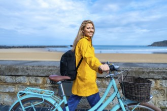 Tourist walking with her bicycle along the beach wall on a cloudy day, enjoying the fresh air and