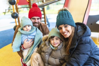 Smiling family wearing winter clothes and woolen hats, spending time together at the playground