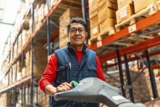 Low angle view portrait of a cheerful latin warehouse worker using machinery