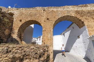 A man walks through an arch under a historic aqueduct in the white village of Yunquera, Sierra de