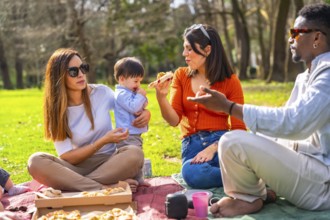 Family and friends enjoying pizza while picnicking in a vibrant green park, laughing and sharing