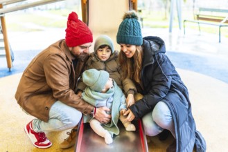 Parents assisting their children as they joyfully slide down a playground slide, embracing the fun