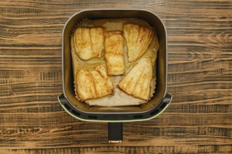 Five golden brown grilled fish fillets are neatly placed inside an air fryer basket. The background