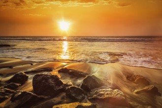 Tropical beach vacation background, waves and rocks on beach on sunset with beautiful cloudscape.