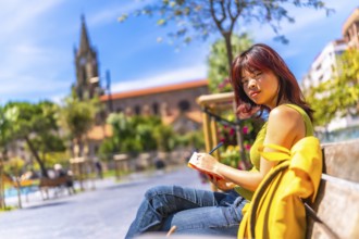 Asian cool young woman sketching sitting on a bench in the city in a sunny day