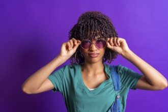 Stylish young woman lowering her purple sunglasses while posing in a vibrant purple studio,