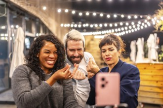 Multiracial diverse friends streaming online with a smartphone and gesturing love during night