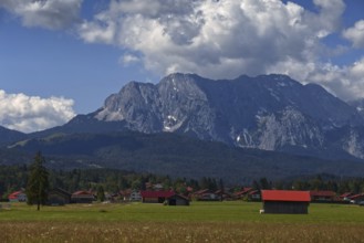 A mountain landscape with a village in the foreground, surrounded by meadows and mountains under a