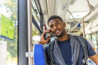 African young man talking to the mobile sitting in an urban bus