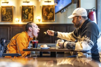 Caregiver tenderly feeds a disabled man in a restaurant, highlighting the importance of support,