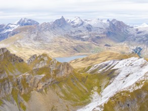 Expansive mountain landscape with snow-capped peaks, valleys and a small lake in the background,