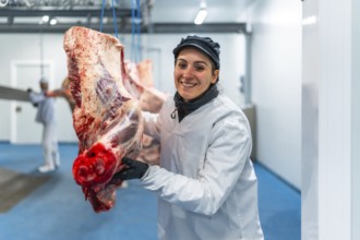 Happy female butcher carrying meat hanging in cold store of a slaughterhouse