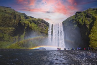 Group of tourists looking at the beautiful rainbow at the impressive Skogarfoss waterfall in