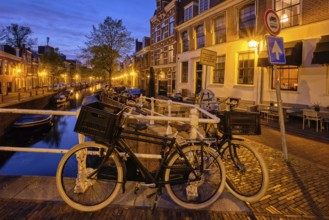 Typical Netherlands cityscape, bycicle at canal with boats and houses illuminated in the evening.