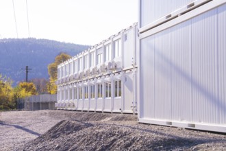 Row of white containers along a gravel path, illuminated by sunlight, refugee accommodation